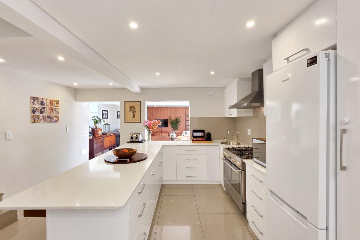 Modern kitchen featuring white cabinetry, quartz countertops, gas hob, stainless steel extractor, and tiled flooring, with an open-plan layout connecting to the living area.