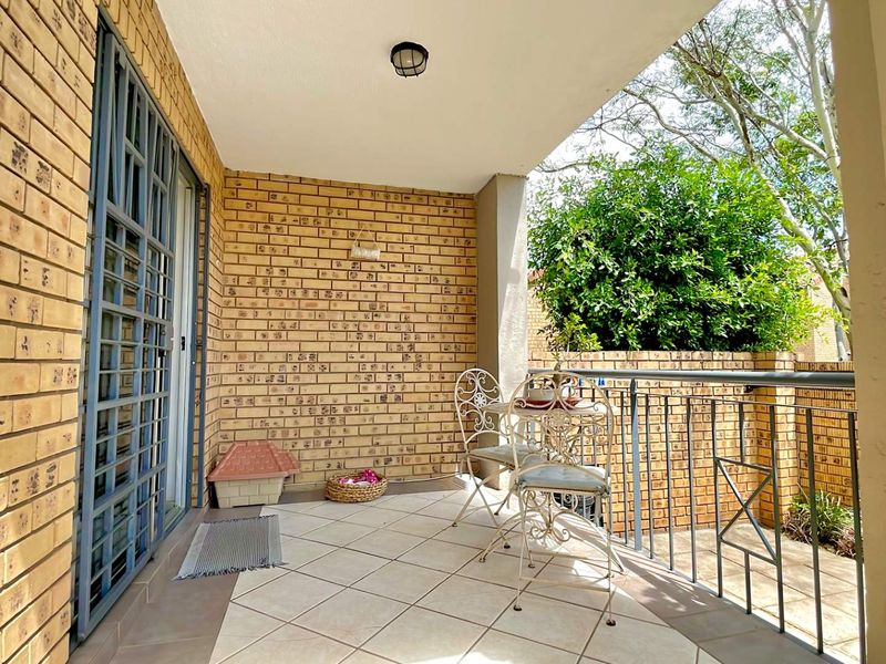A covered patio area featuring face-brick walls, tiled flooring, and metal security gate access, providing a functional outdoor space.