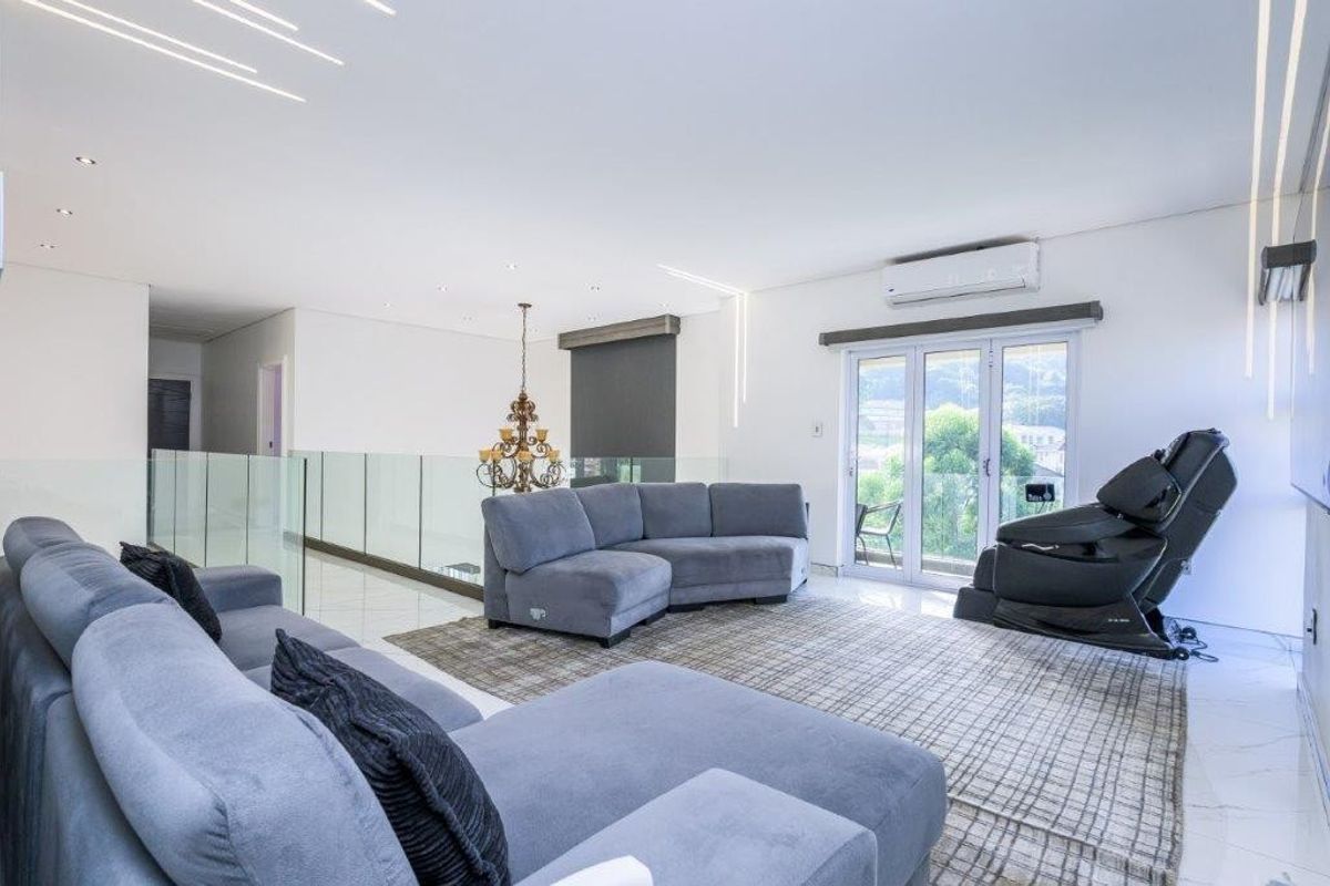 Modern, bright living room featuring sleek tiled flooring, recessed lighting, a glass balustrade, and direct access to an outdoor balcony through french doors.