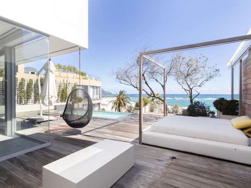 Spacious outdoor timber deck featuring a private swimming pool, glass facade, and panoramic ocean views, perfect for coastal living.