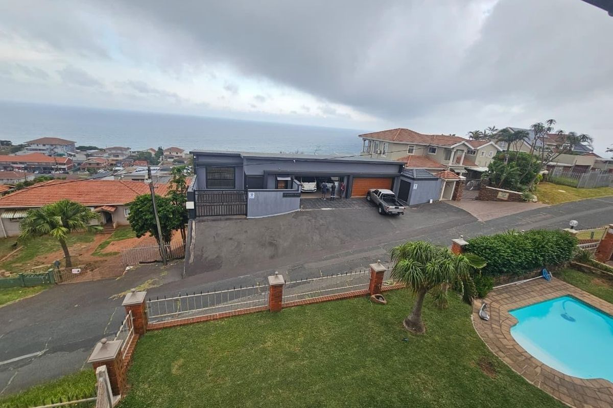 Aerial view of the property featuring a swimming pool, landscaped garden, paved driveway, and garage, with a scenic coastal outlook.