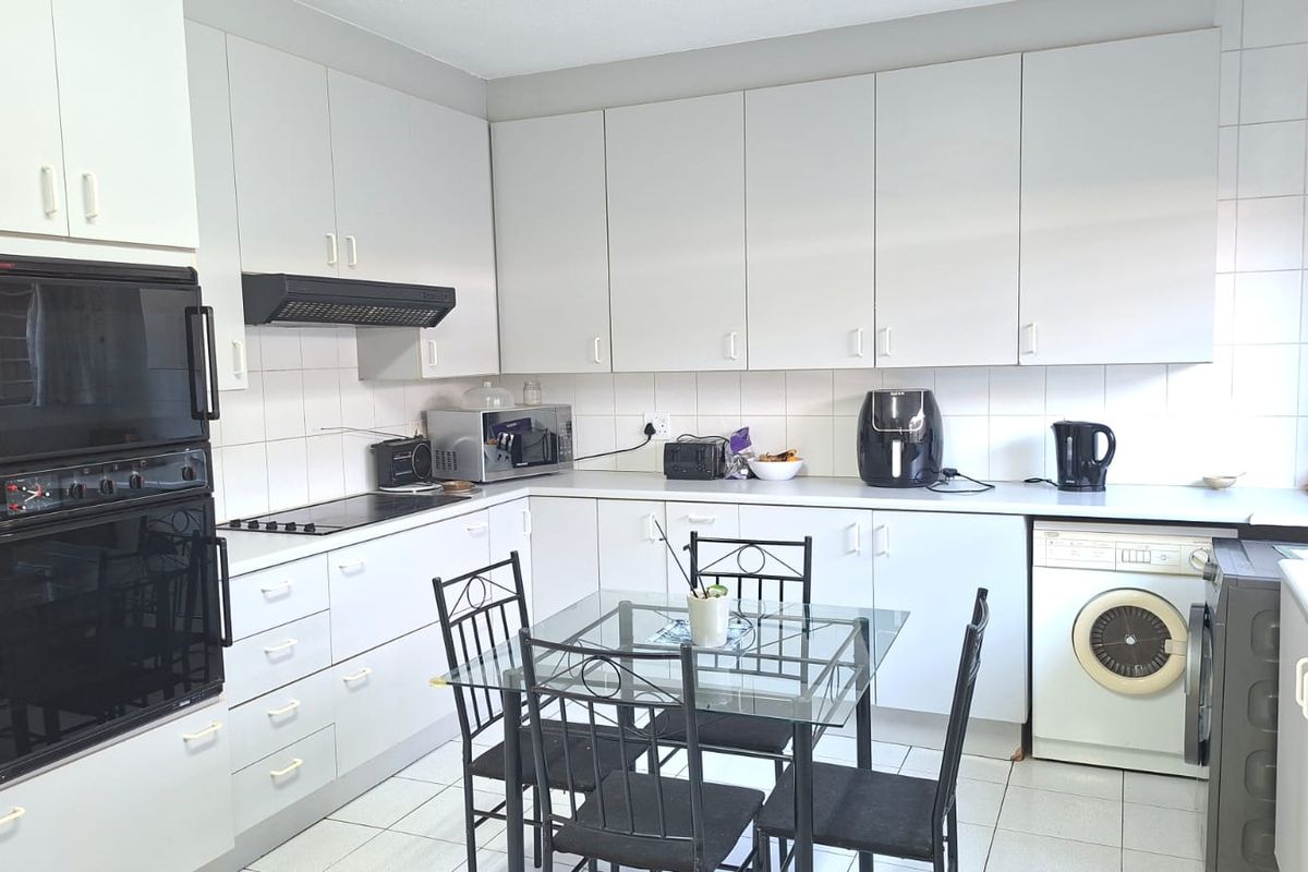 Functional kitchen featuring white cabinetry, built-in double oven, electric hob, extractor fan, and tiled splashback with integrated laundry space.