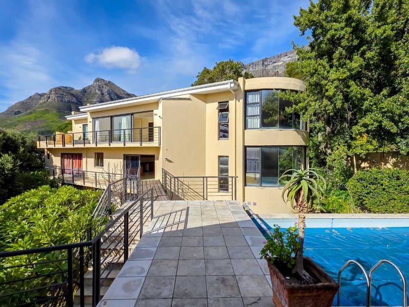 Rear exterior view featuring a swimming pool, tiled patio area, elevated walkway, and a distinctive curved architectural facade set against a mountain backdrop.