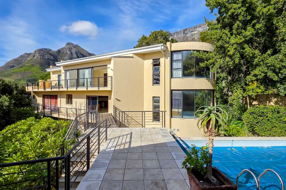 Rear exterior view featuring a swimming pool, tiled patio area, elevated walkway, and a distinctive curved architectural facade set against a mountain backdrop.