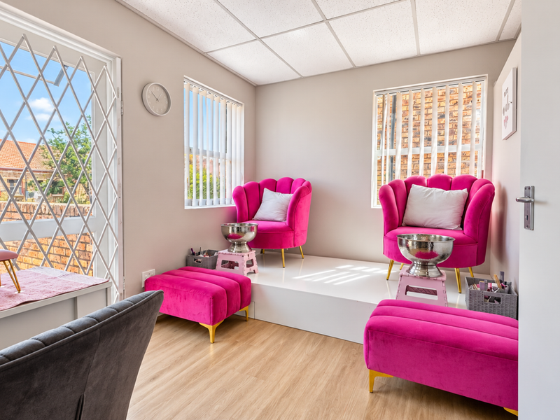 A bright, well-maintained commercial space featuring a raised platform, laminate flooring, vertical blinds, and a secure entrance gate, ideal for a salon or office.