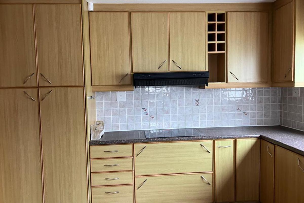A functional kitchen featuring light wood-look laminate cabinetry, a tiled backsplash, integrated extractor fan, and a dark laminate countertop with an electric cooktop.
