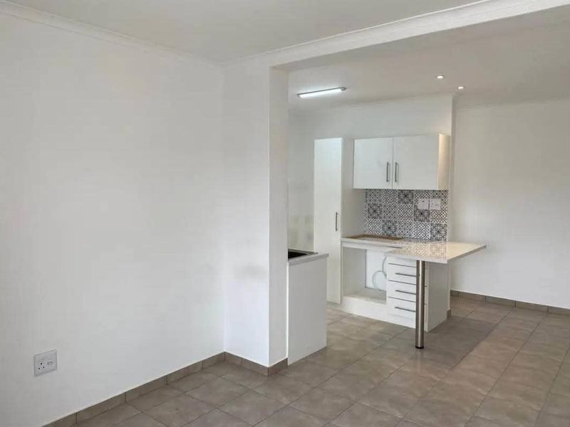 An open-plan living and kitchen area featuring neutral tiled flooring, modern white cabinetry, a patterned tile backsplash, and a functional breakfast bar.
