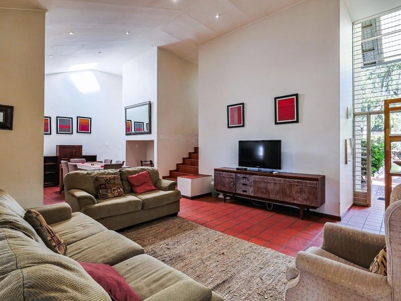 Spacious open-plan living and dining area featuring vaulted ceilings, a skylight, terracotta tile flooring, and direct access to an outdoor space via a security gate.