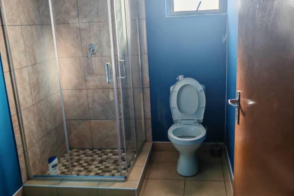 A functional bathroom featuring a glass-enclosed shower with tiled walls and a standard toilet, finished with neutral floor tiles.