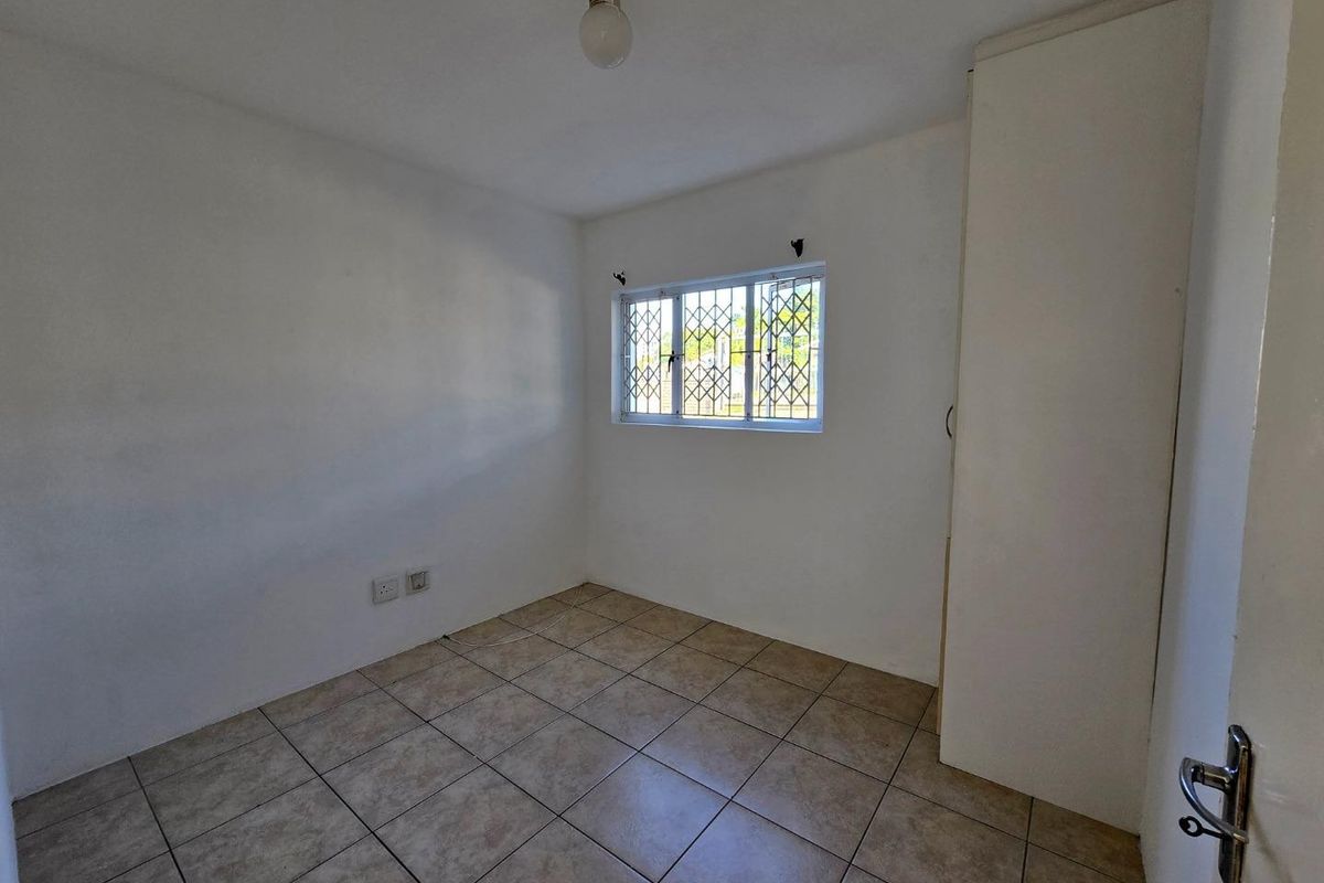 A clean, empty bedroom featuring tiled flooring, a built-in wardrobe, and a window fitted with a security gate.