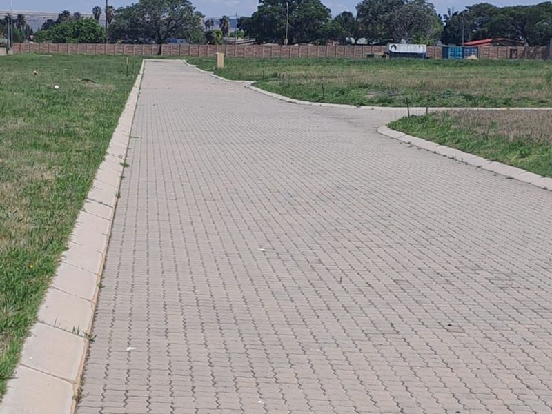 A clear view of a paved residential driveway and access road leading into a vacant land plot with established boundary walling.