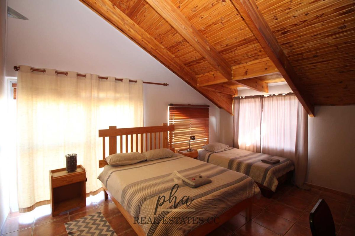 A bedroom featuring a vaulted timber-clad ceiling, tiled flooring, and large windows allowing for natural light.