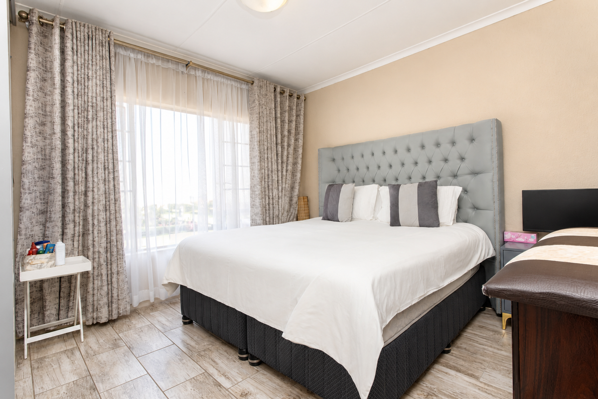 A well-maintained bedroom featuring tiled flooring, large windows with curtain tracks, and neutral wall finishes.