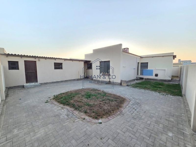 A rear exterior view of the property featuring a paved courtyard area with a central garden bed and surrounding boundary walls.