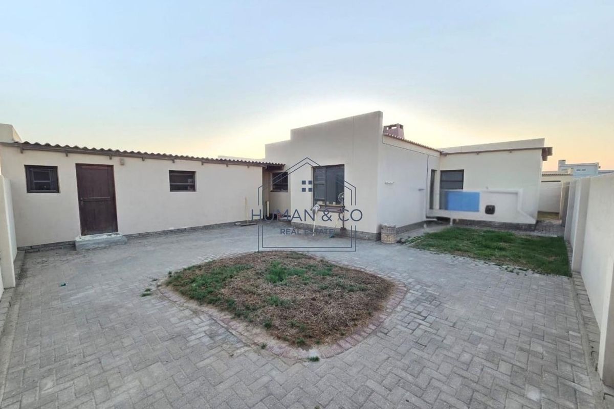 A rear exterior view of the property featuring a paved courtyard area with a central garden bed and surrounding boundary walls.