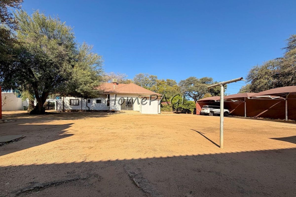 Spacious rear yard featuring a large open area, a covered carport, and a tiled roof dwelling with security bars on windows.