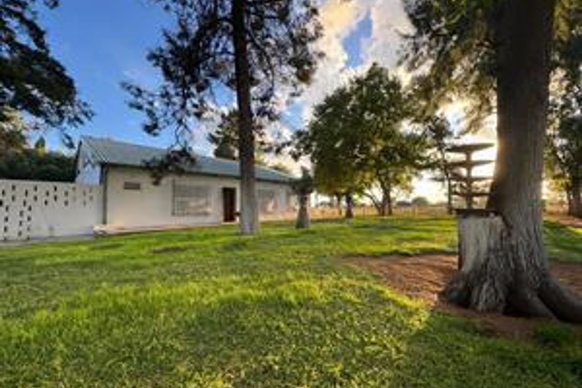A view of the farm property exterior featuring a well-maintained lawn, mature trees, and the main building structure with a metal roof.