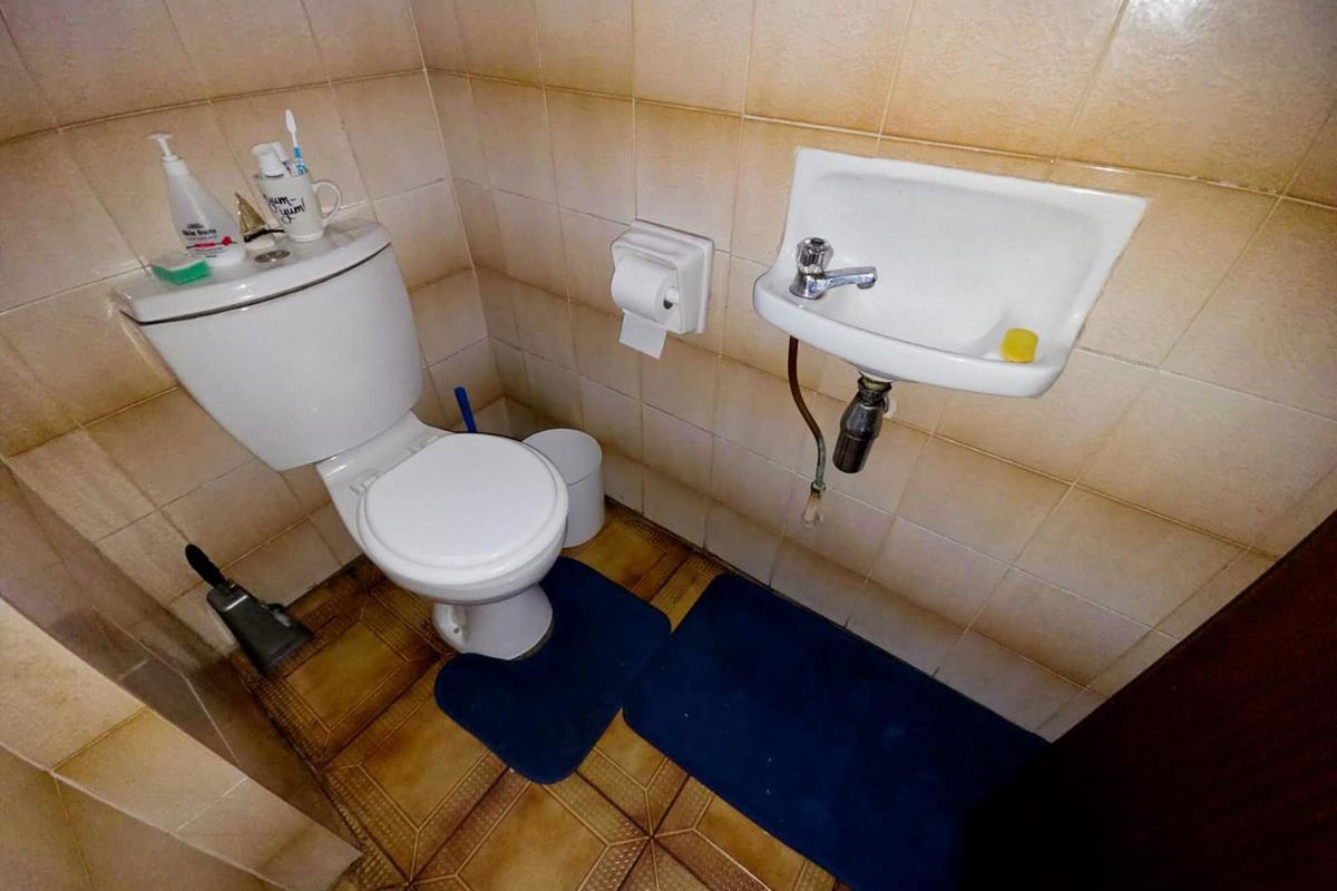 A compact guest cloakroom featuring a standard toilet and a small wall-mounted basin with tiled walls and flooring.