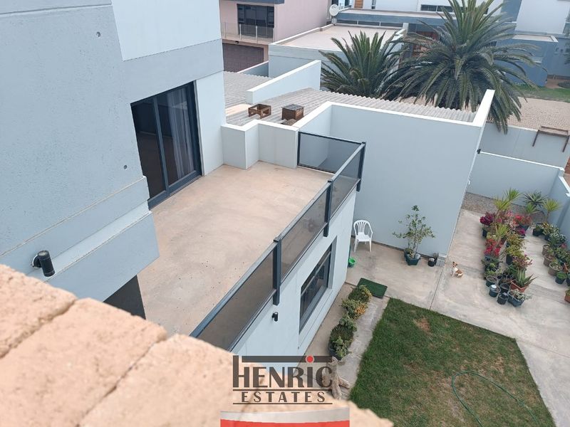 An elevated view of the rear exterior featuring a modern balcony with glass balustrades, a concrete patio area, and a small private garden.