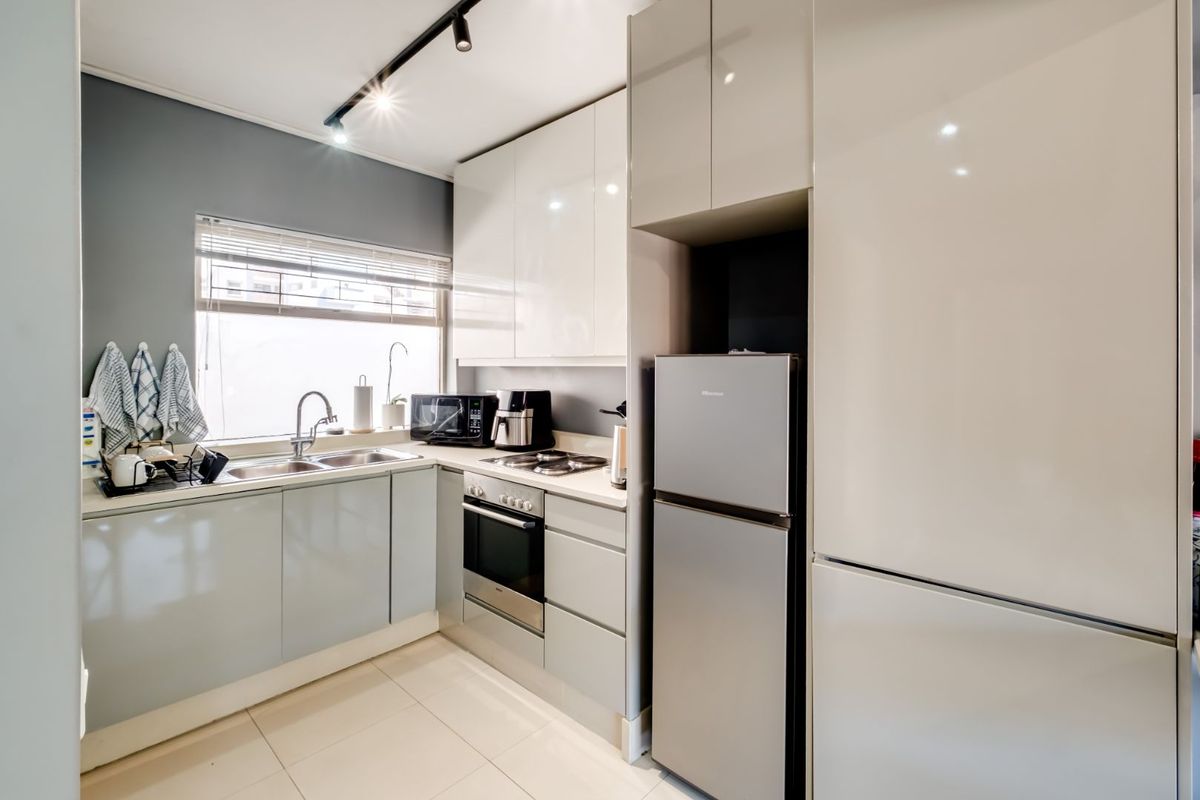 Modern kitchen featuring high-gloss cabinetry, integrated oven, hob, and stainless steel sink with tiled flooring and track lighting.