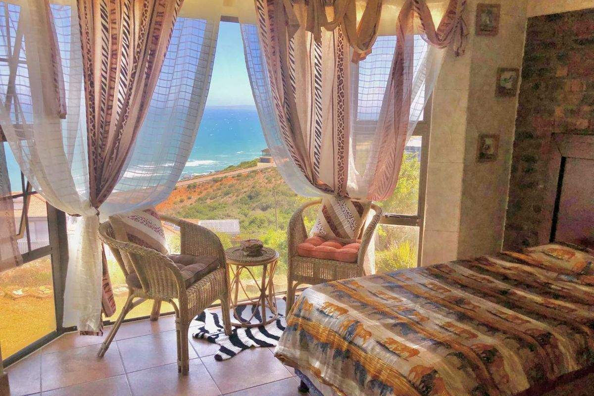 A bedroom featuring large windows with expansive coastal views, tiled flooring, and a stone-accented wall.