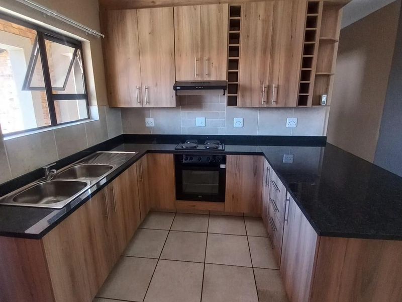 A clean, modern kitchen featuring wood-finish cabinetry, granite countertops, a built-in oven with hob, and tiled flooring, offering a functional and well-maintained workspace.
