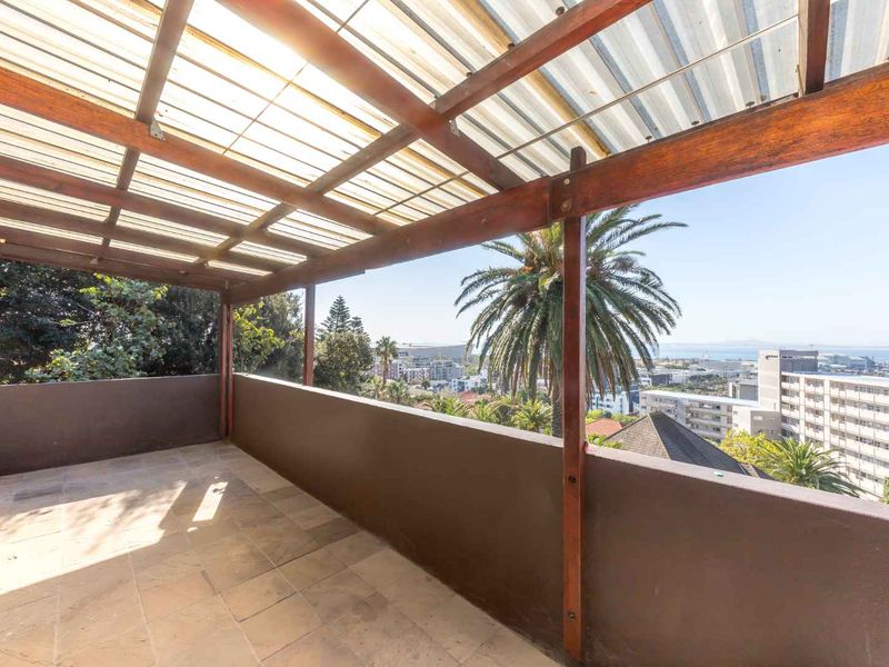 Spacious covered balcony featuring a timber pergola, tiled flooring, and panoramic urban and coastal views.