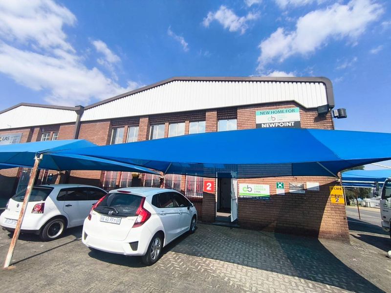 Front exterior view of an industrial unit featuring a brick facade, metal roofing, and a large blue shade cloth carport over the paved entrance area.