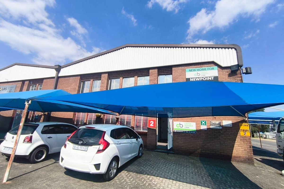 Front exterior view of an industrial unit featuring a brick facade, metal roofing, and a large blue shade cloth carport over the paved entrance area.