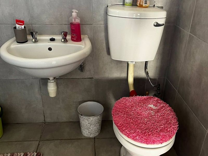 A compact bathroom featuring a wall-mounted basin and a standard ceramic toilet with grey wall and floor tiling.