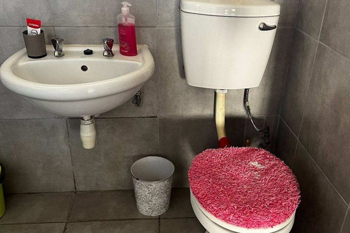A compact bathroom featuring a wall-mounted basin and a standard ceramic toilet with grey wall and floor tiling.