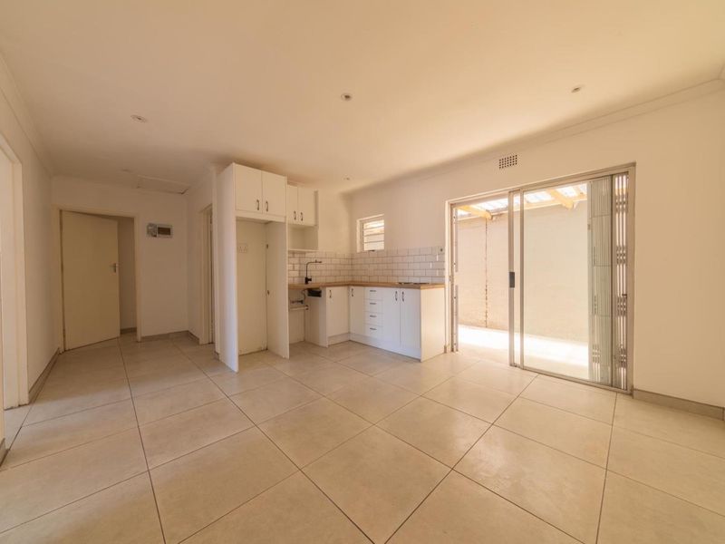 An open-plan living and kitchen area featuring tiled floors, white cabinetry, subway tile backsplash, and direct access to an outdoor patio through sliding doors.