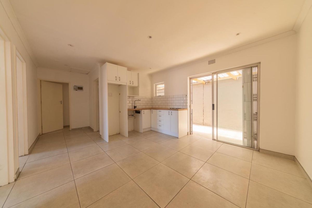 An open-plan living and kitchen area featuring tiled floors, white cabinetry, subway tile backsplash, and direct access to an outdoor patio through sliding doors.