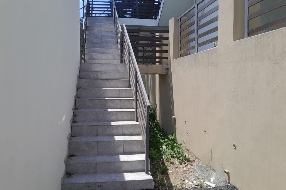 Exterior staircase with tiled steps and metal railings leading to an elevated walkway, situated between retaining walls.