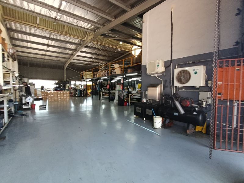 Spacious industrial warehouse featuring a mezzanine level, high-clearance exposed steel roof, durable epoxy flooring, and integrated air conditioning and compressor systems.