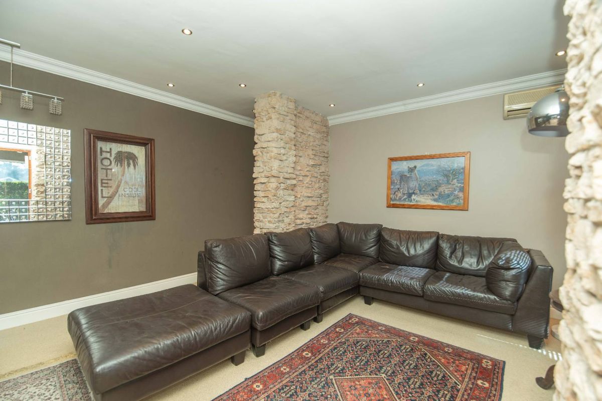 A comfortable living room featuring a distinctive stone pillar, recessed ceiling lighting, crown molding, and a wall-mounted air conditioning unit.