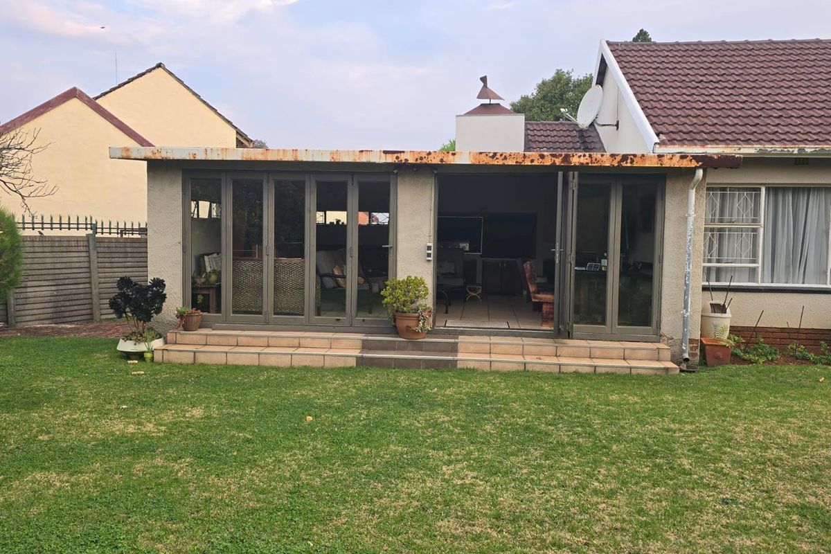 Rear view of the property featuring a tiled patio with aluminium stacker doors leading into the living area and a large garden.