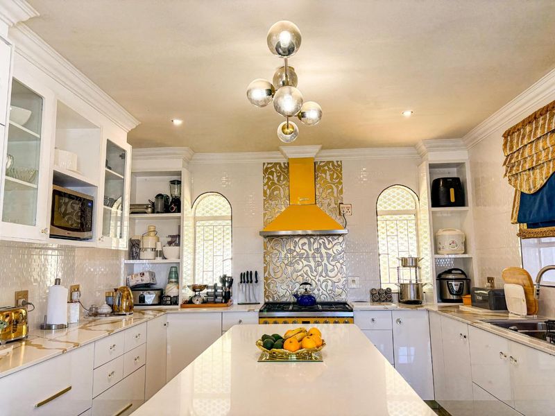 A well-appointed kitchen featuring white cabinetry, quartz countertops, a central island, and a distinctive yellow extractor fan with decorative tiled backsplash.