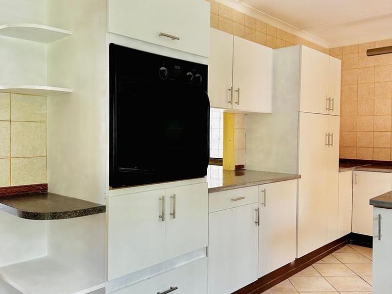 A functional kitchen featuring white built-in cabinetry, a wall-mounted oven, tiled backsplash, and ceramic floor tiles, offering a clean and practical layout.