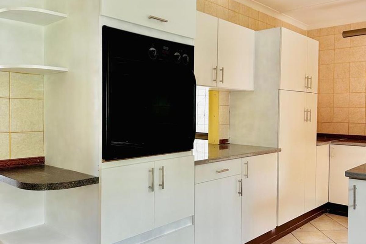 A functional kitchen featuring white built-in cabinetry, a wall-mounted oven, tiled backsplash, and ceramic floor tiles, offering a clean and practical layout.