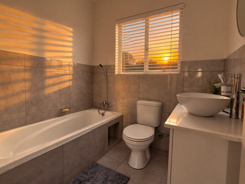 A modern bathroom featuring a bathtub with handheld shower, a white toilet, and a vessel sink set on a vanity cabinet with tiled finishes.