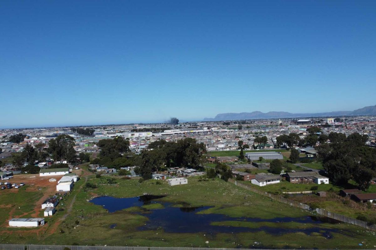 An aerial view of a large, undeveloped agricultural plot featuring open land, patches of standing water, and surrounding residential and commercial infrastructure.