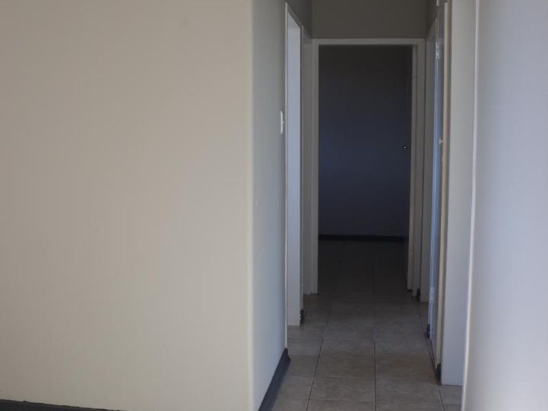 A clean, empty hallway featuring neutral wall paint and ceramic floor tiles, providing access to adjacent rooms within the apartment.