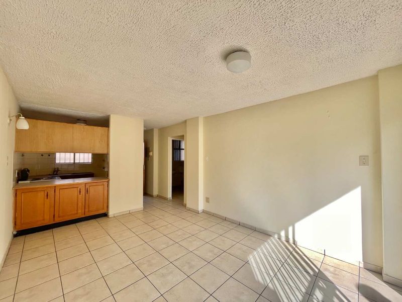 Open plan living area featuring tiled flooring and a compact kitchen with built-in cabinetry, offering a blank canvas for renovation.