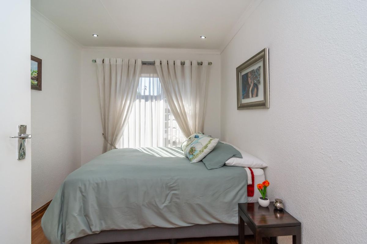A well-maintained bedroom featuring laminate flooring, recessed downlighting, and a window with curtains, providing a comfortable and functional living space.