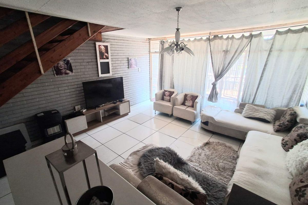 Spacious living room featuring tiled flooring, an exposed brick wall, a wooden staircase, and large glass sliding doors leading to the exterior.