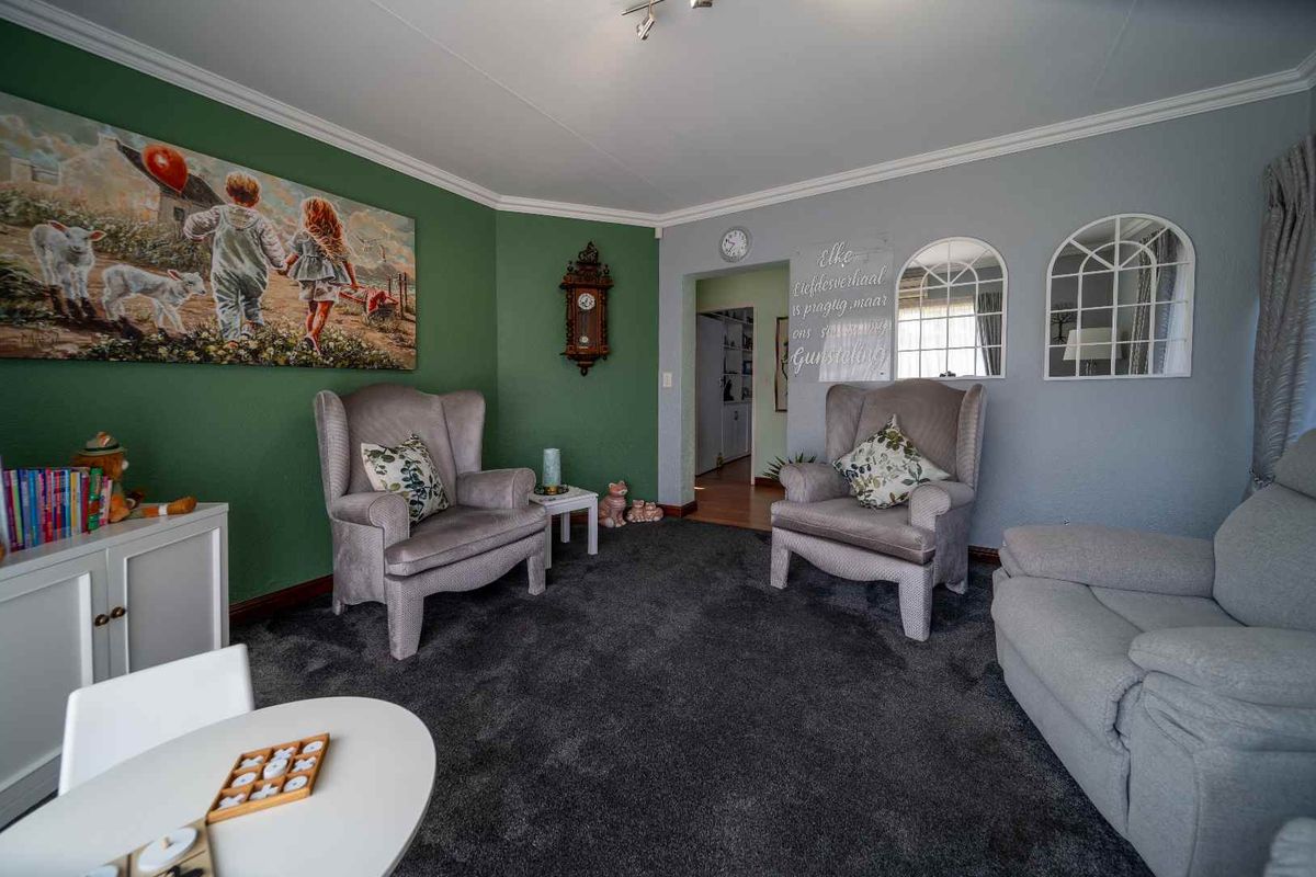A cozy living room featuring dark carpeting, contrasting green and grey painted walls, and arched wall mirrors.