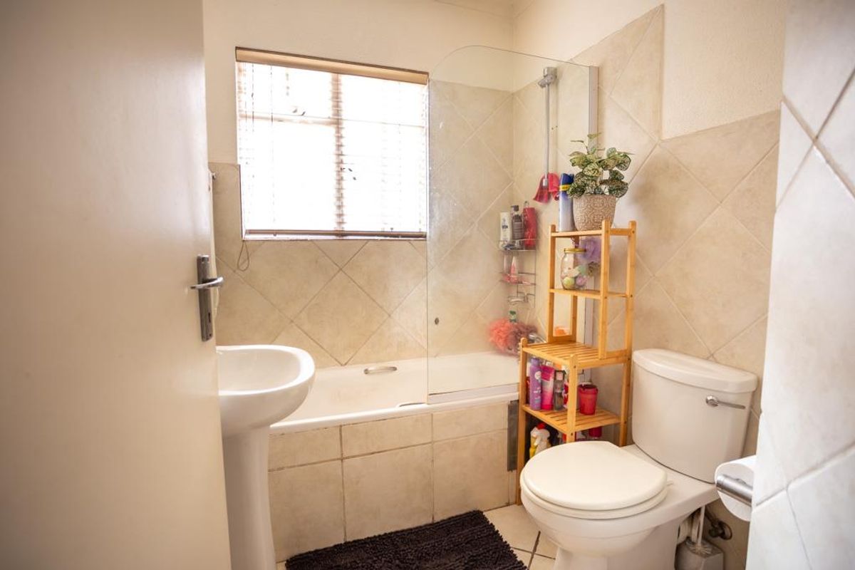 A functional bathroom featuring a pedestal basin, a toilet, and a bathtub with a glass shower screen and tiled splashbacks.