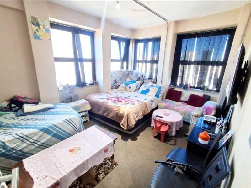 A bedroom featuring large windows providing natural light, with visible exposed electrical conduit and dated flooring finishes.