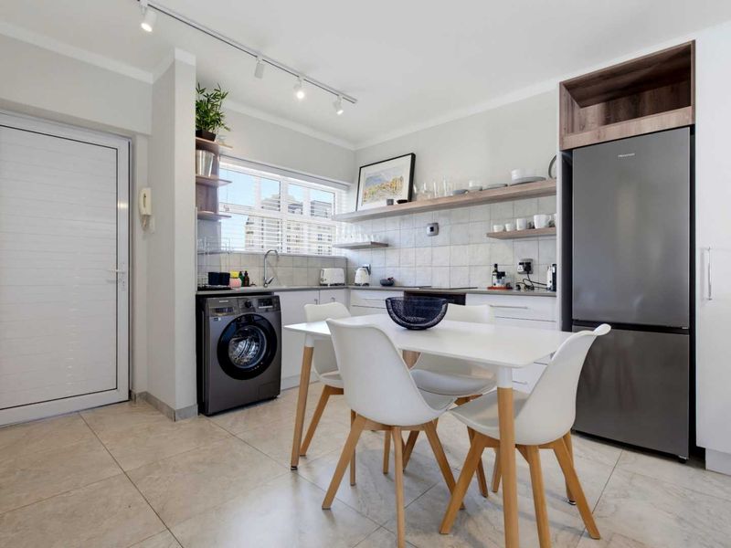 Modern open-plan kitchen and dining area featuring tiled floors, sleek cabinetry, open shelving, and integrated appliances in a well-maintained apartment setting.